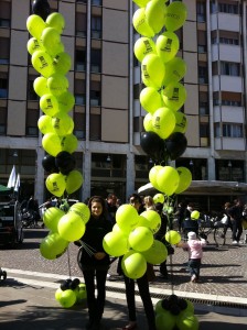 due hostess per un'azione di Guerrilla Marketing con palloncini tengono in mano due ciuffi enormi di palloncini stampati verdi e neri